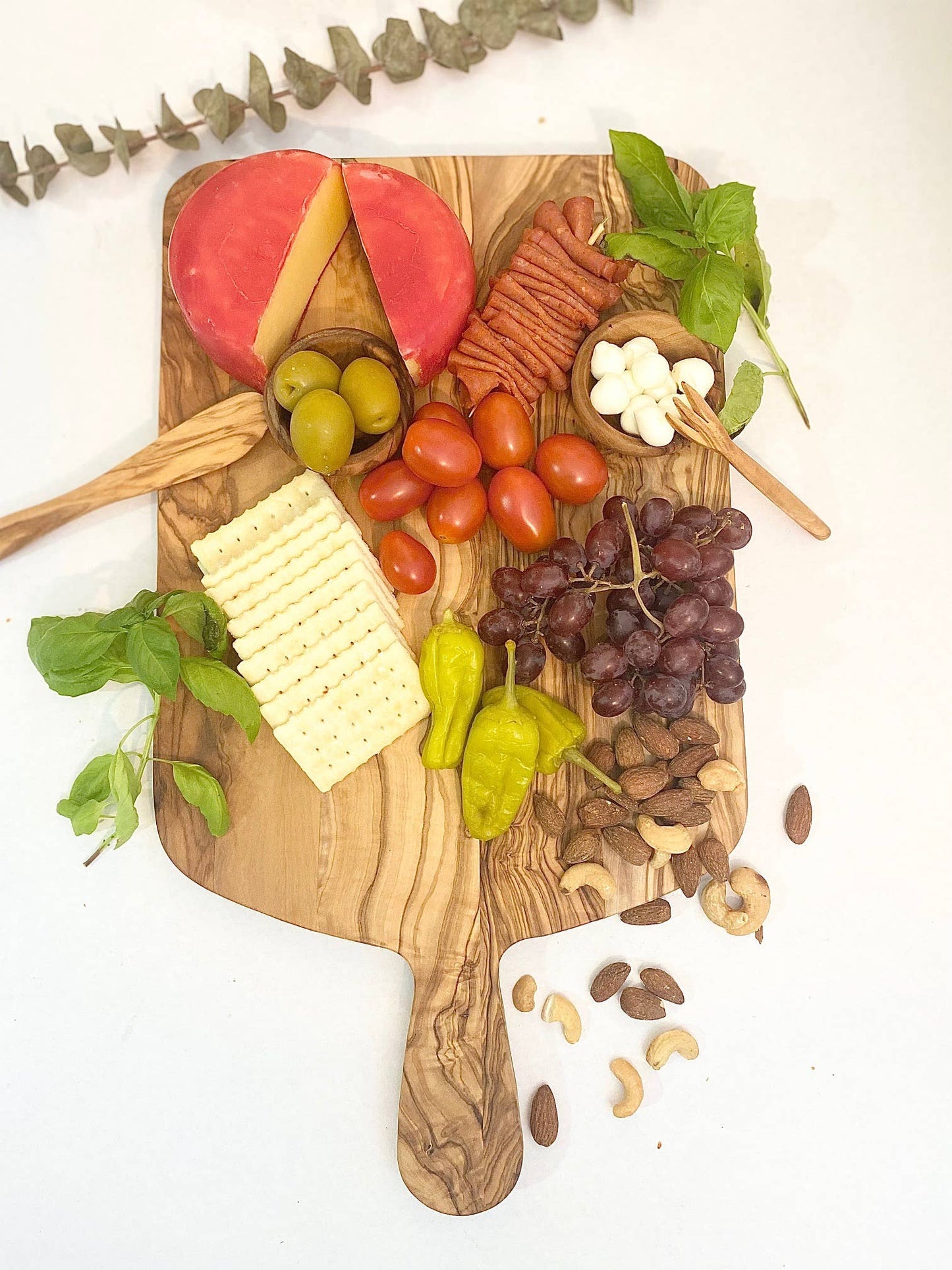 Overhead view of an olive wood charcuterie board beautifully arranged with an assortment of cheeses, meats, fruits, and nuts. This stylish and sustainable board is perfect for hosting gatherings and adding a touch of elegance to your next party or event. The natural wood grain of the olive wood enhances the presentation, making it an eye-catching centerpiece for any occasion. Ideal for those who appreciate quality, craftsmanship, and a delicious spread.