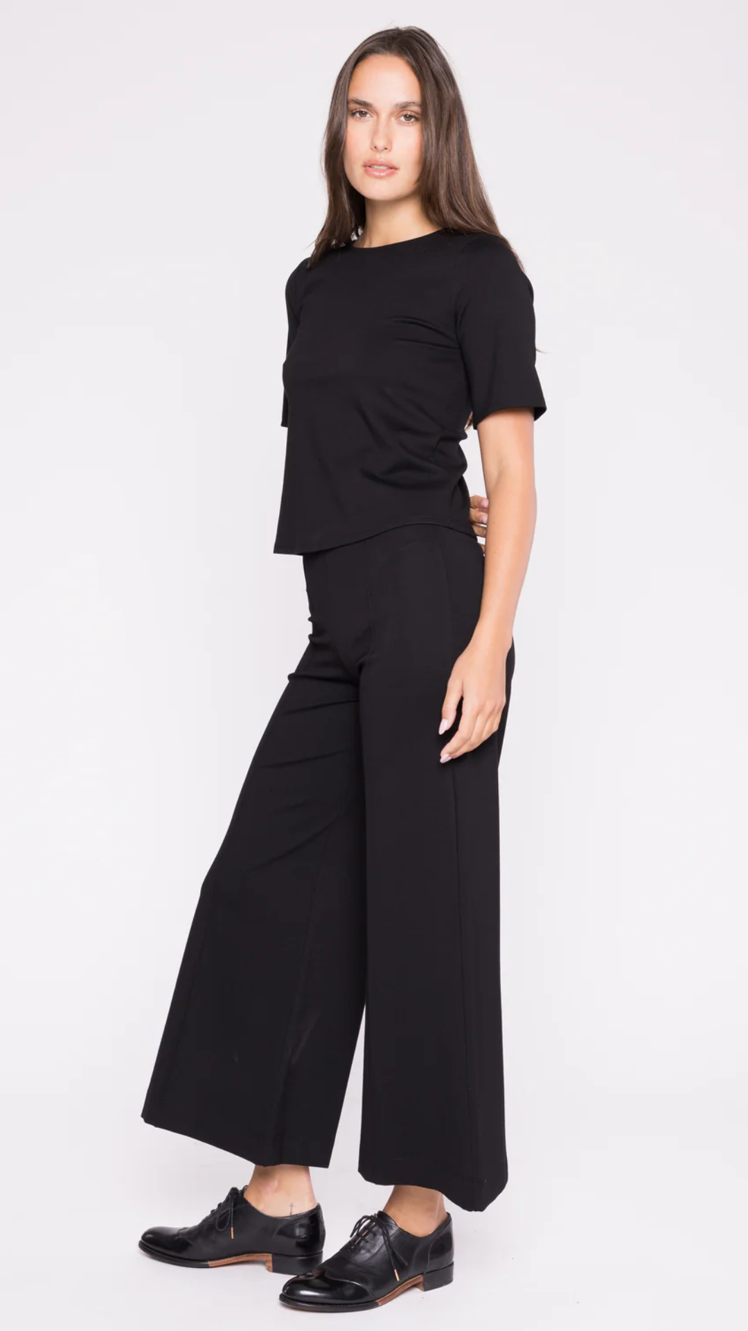 Side view of the model in the Ripley Rader Black Ponte Knit Short Sleeve Top, showcasing its extended length, flattering silhouette, and premium American-made craftsmanship for timeless elegance.