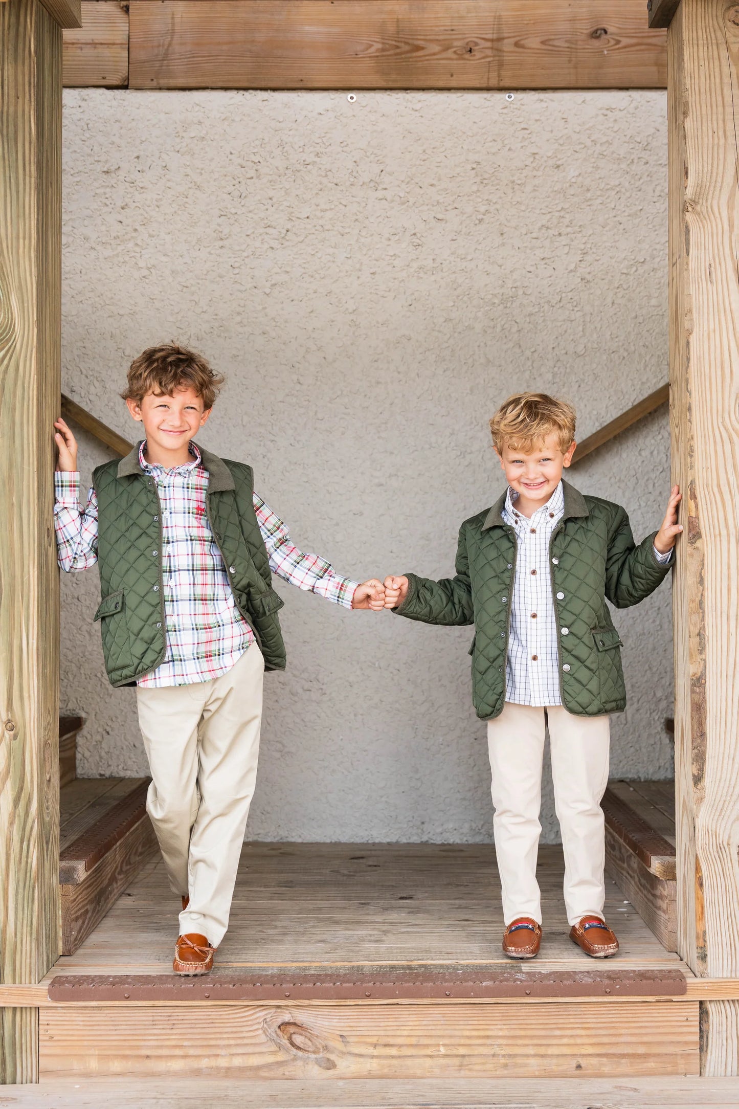 Two boys holding hands in doorway, one wearing Boys Derby Field Jacket with performance pants, the other in Saltwater Boys best sellers, highlighting coordinated fall styles for kids.
