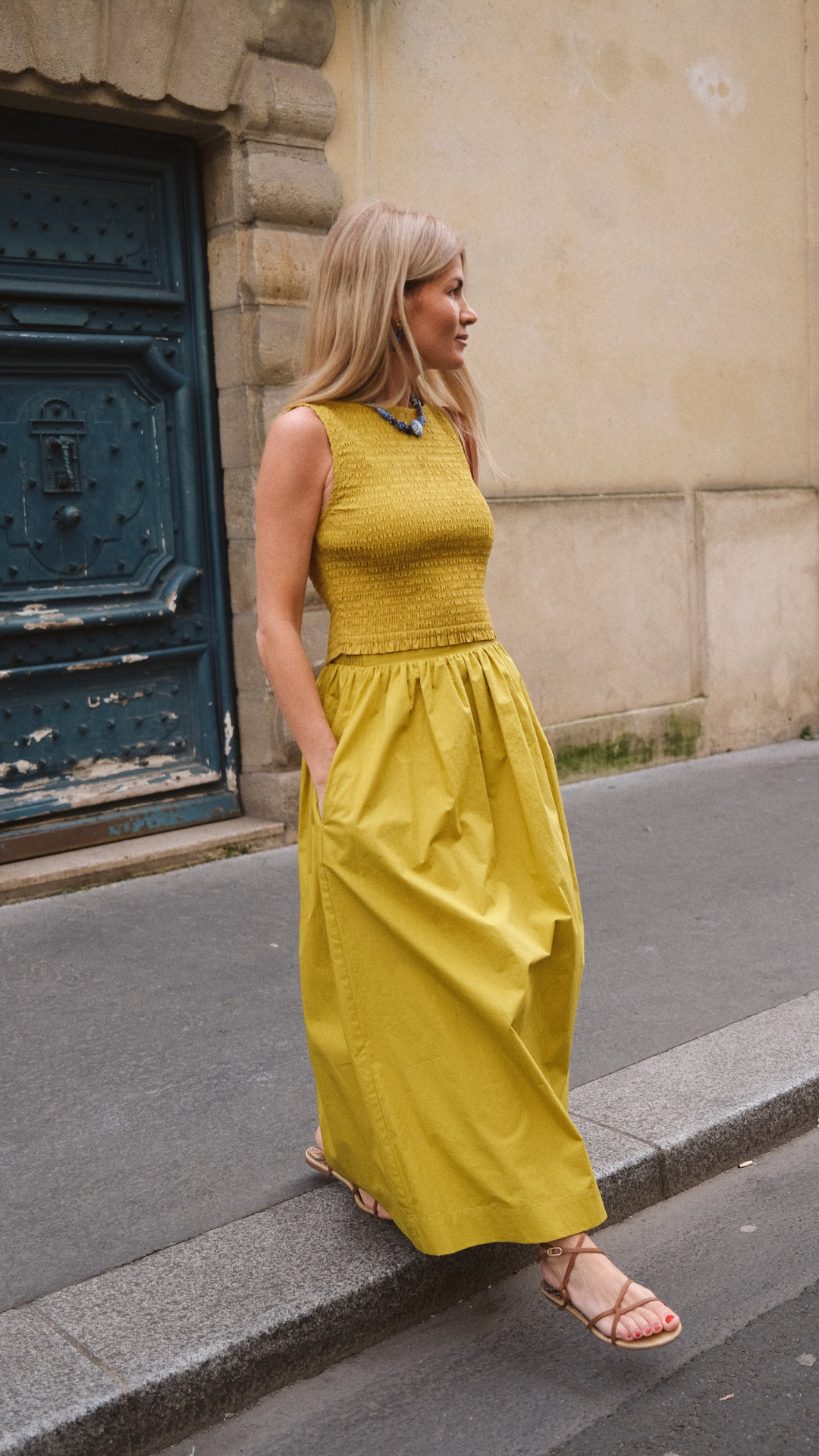 Liz Joy wearing the Charlotte Smocked Top with a matching skirt, walking the streets of Paris in an elegant high-waisted look.