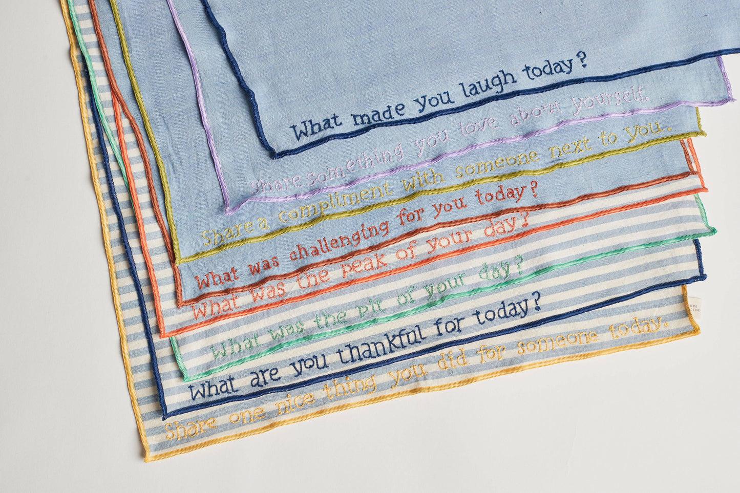 Close-up of a hand-embroidered prompt on one of the conversation napkins, showing fine stitching on chambray fabric