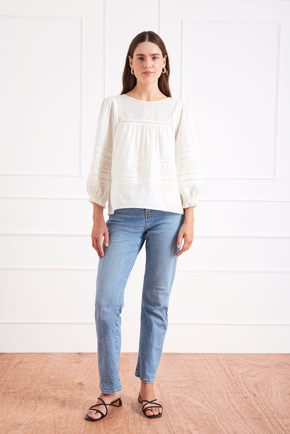 Front studio view of the white Dawn Blouse, featuring delicate pin tucks and lace trim, styled with denim for an effortlessly romantic look.