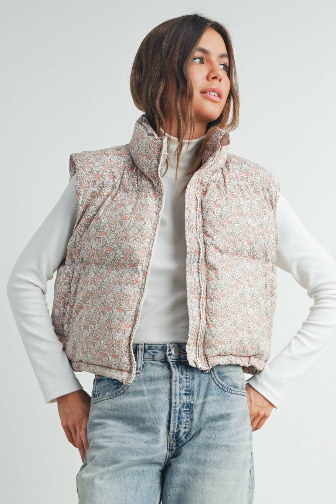 Model smiling over her shoulder while wearing the Floral High Neck Puffer Vest, showing back detail and soft, feminine style