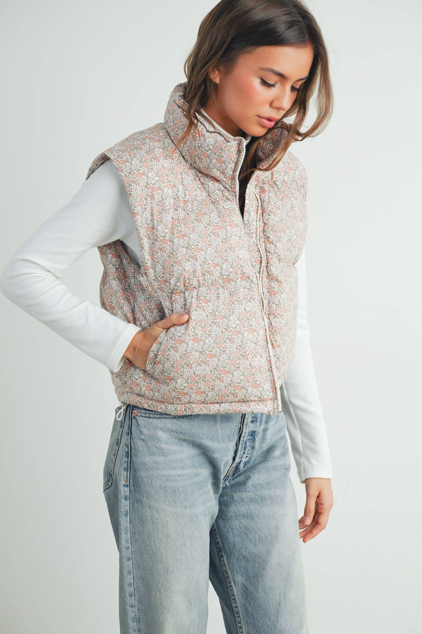 Studio image of model walking forward in floral puffer vest and jeans, showcasing movement and fit