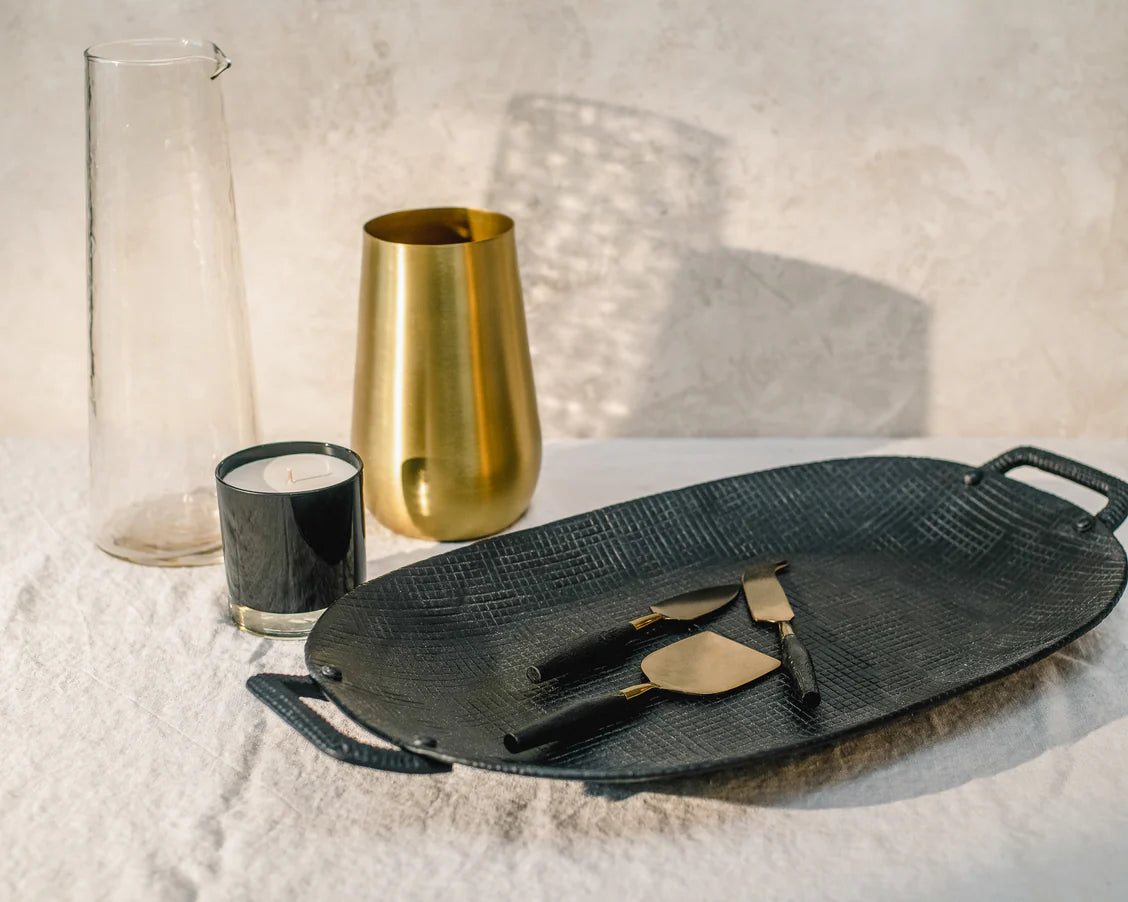 Display of Gather Intentional Living serving and entertaining pieces – featuring a black metal tray, glass pitcher, gold vase, gold & black cheese knives, and hand-poured candle, designed by Kayty Helgersen, a CT local and hospitality specialist. Perfect for stylish hosting and meaningful gatherings.
