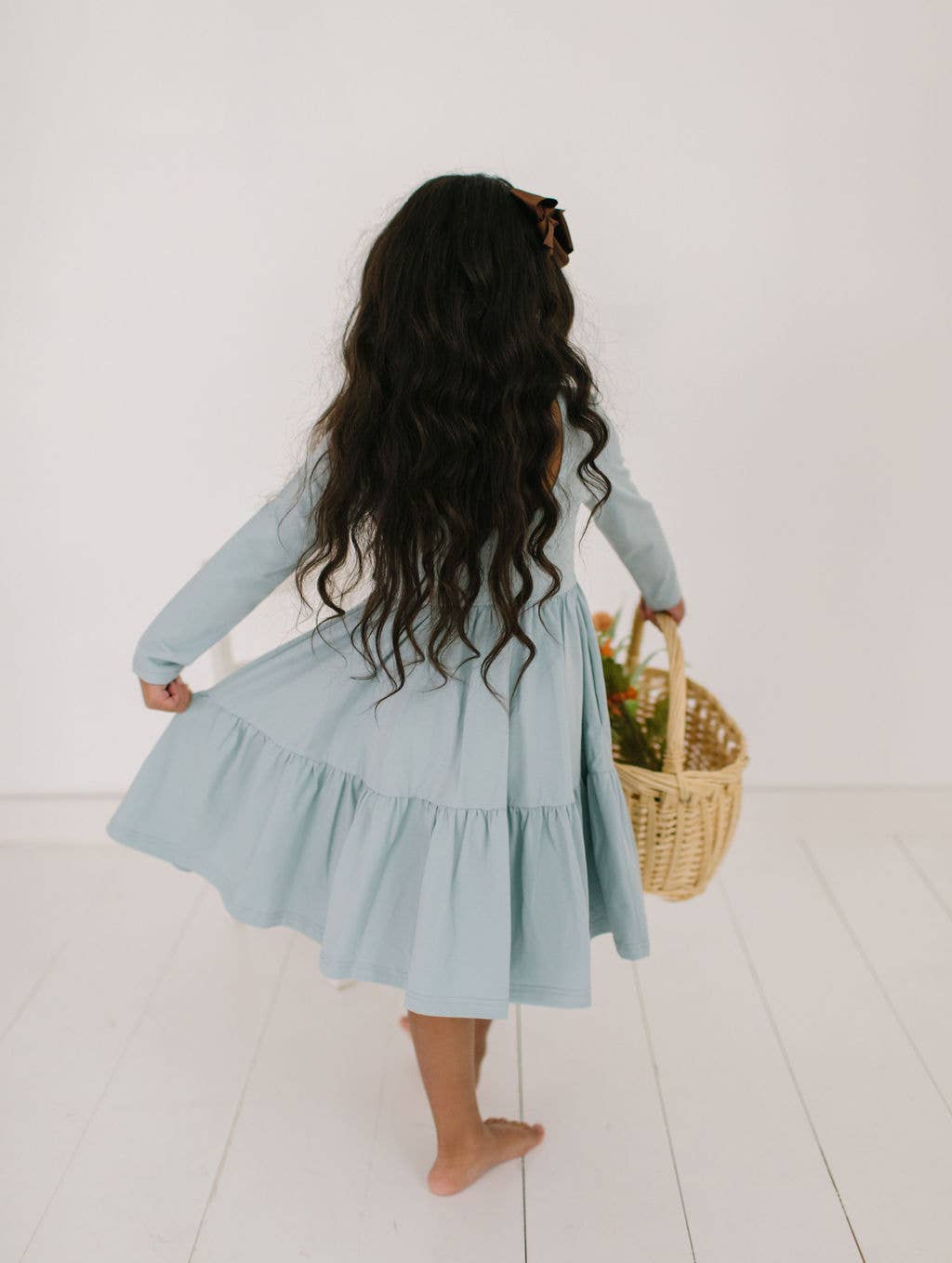 Back view of toddler model holding out the skirt of the Gwendolyn Ruffle Dress in dusty blue, highlighting the playful ruffle details.