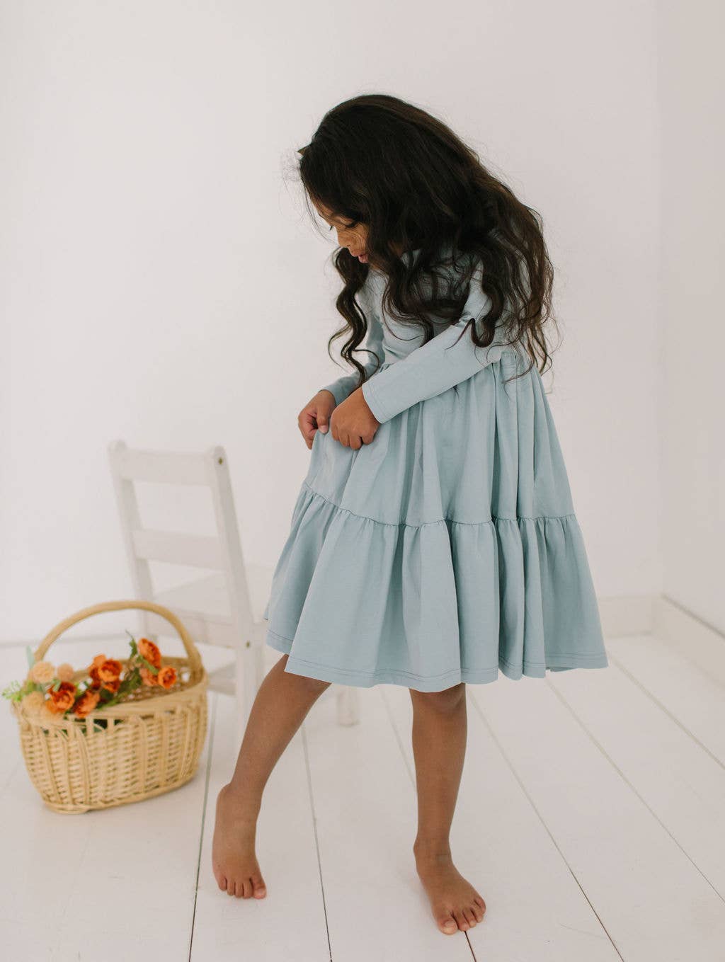 Toddler model showing the hidden pockets of the Gwendolyn Ruffle Dress in dusty blue, perfect for little treasures.