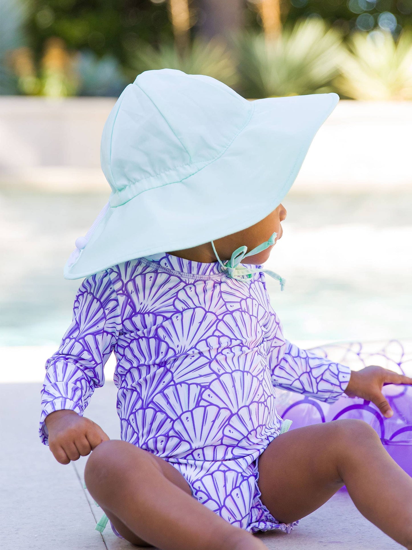 Side profile of baby in mint green sun hat without face visible, showing soft structure and ear coverage