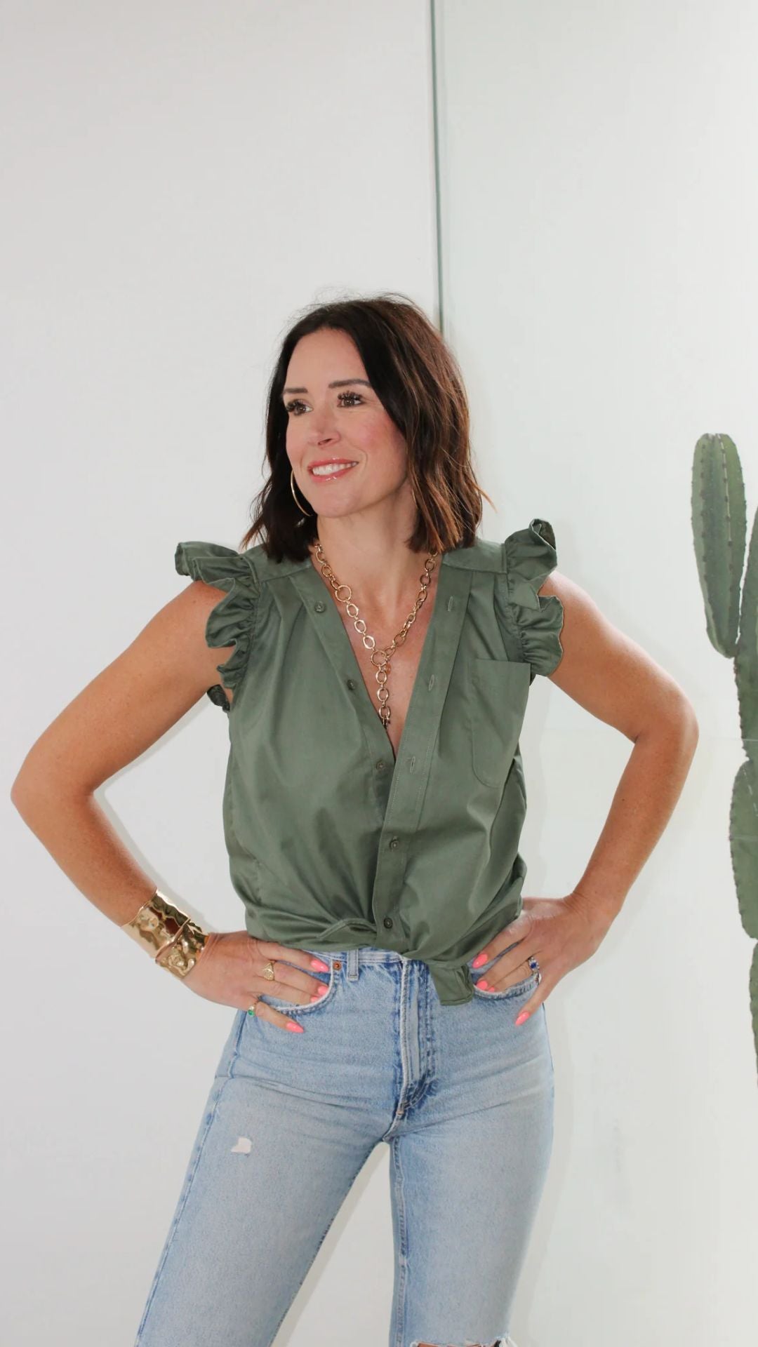 Waist-up studio image of designer Kate in the KMJ Olivia top in Olive, styled with jeans and showcasing the ruffle collar.
