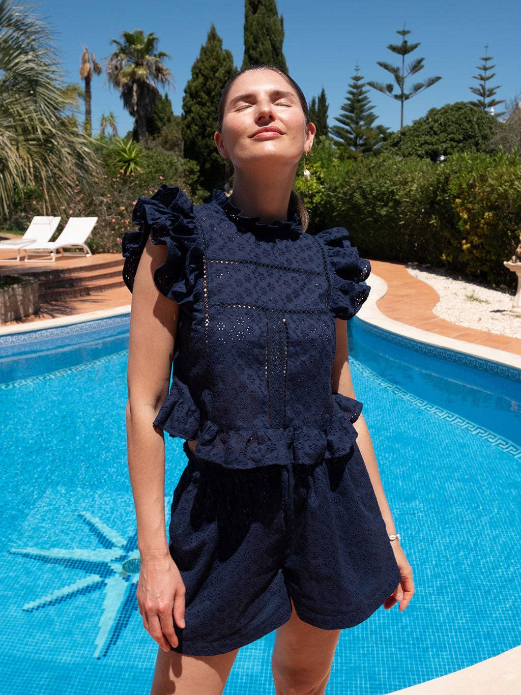 Model standing poolside in the Olivia shorts and Sasha top matching set in navy eyelet, styled for summer.