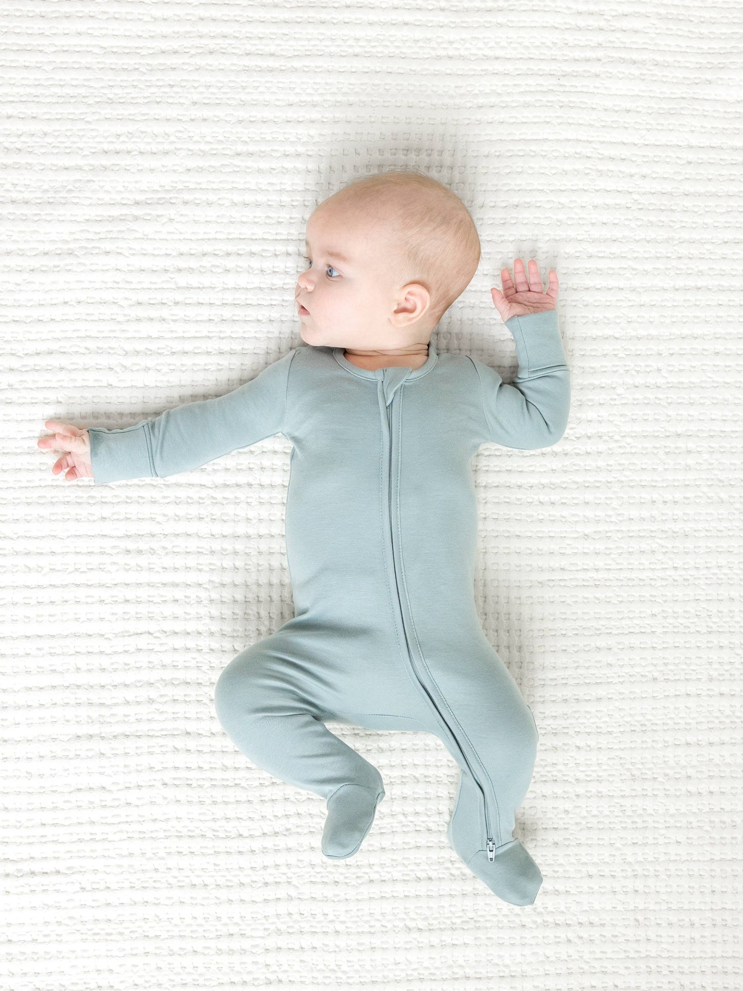 Sweet baby comfortably lying down in the Organic Cotton Zipper Footed Sleeper, made from ultra-soft, breathable organic cotton for a gentle touch on delicate skin.