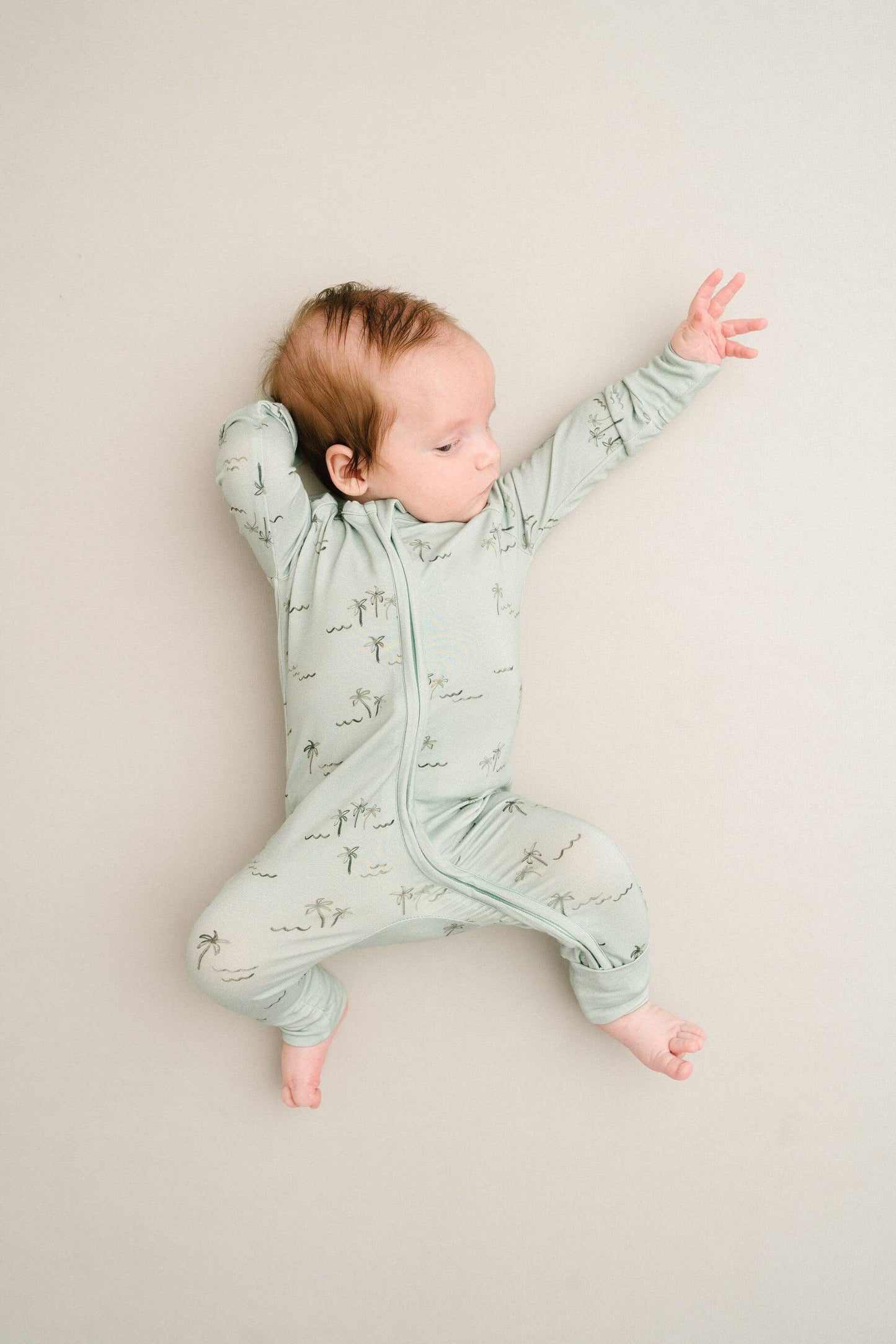 Baby laying on back in crib wearing Palm Breeze Bamboo Sleeper, arms stretched out comfortably.