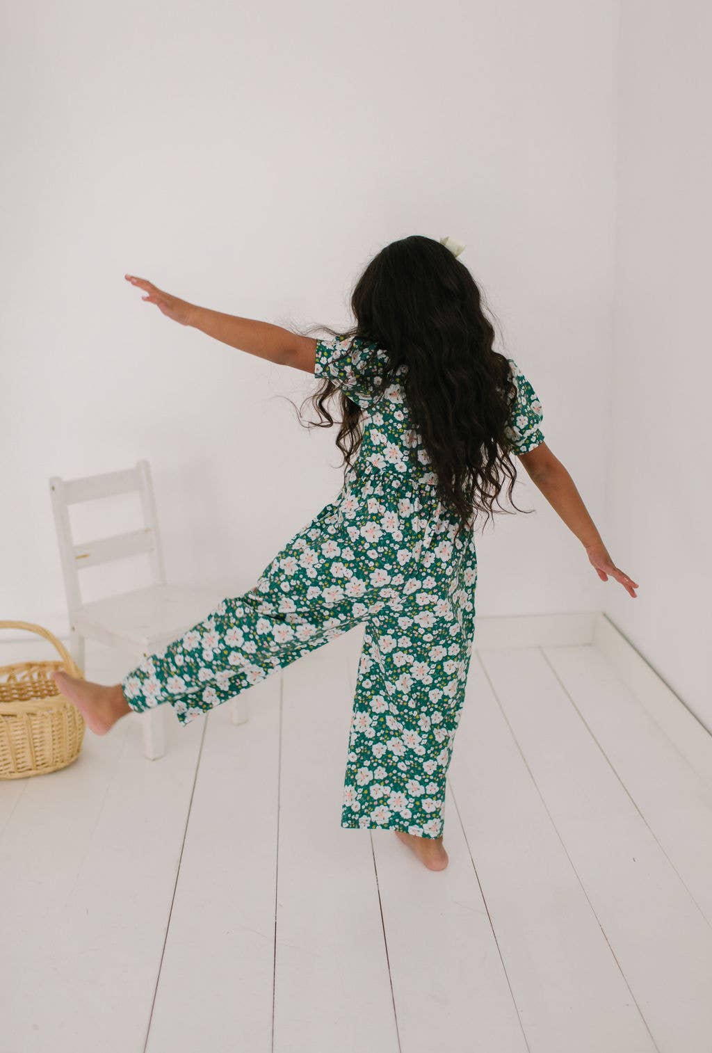 Toddler model with leg out in the puff sleeve romper to show the fullness and soft drape of the cotton blend and wide leg from the back.