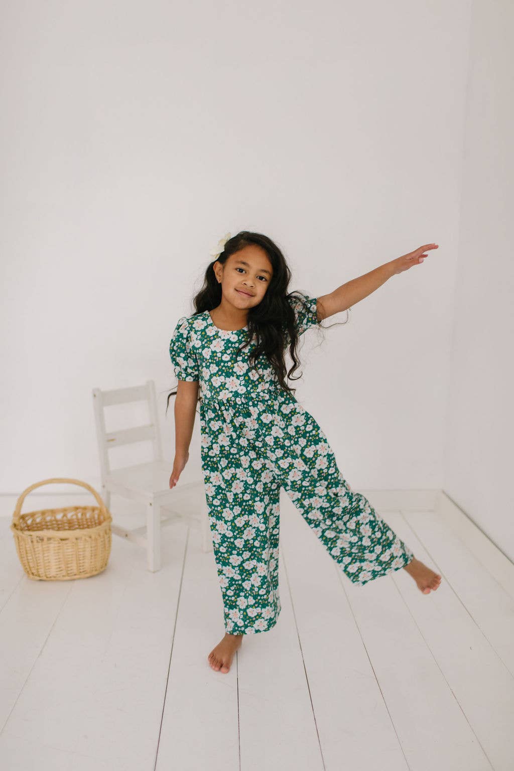 Toddler model with leg out in the puff sleeve romper to show the fullness and soft drape of the cotton blend and wide leg.