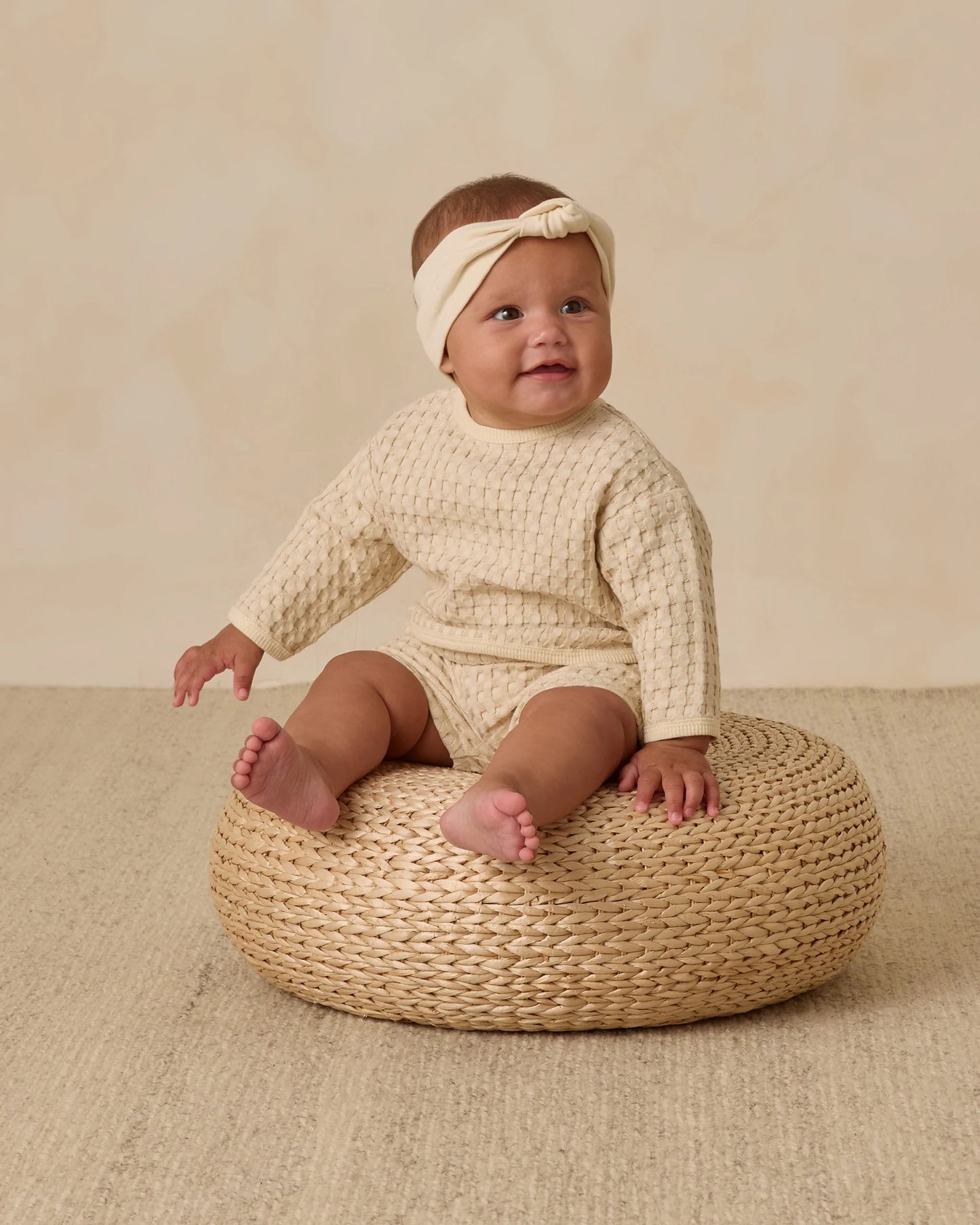 Baby girl in Quincy Mae Flynn Set natural chunky waffle knit, sitting to highlight cozy, breathable design and relaxed fit.