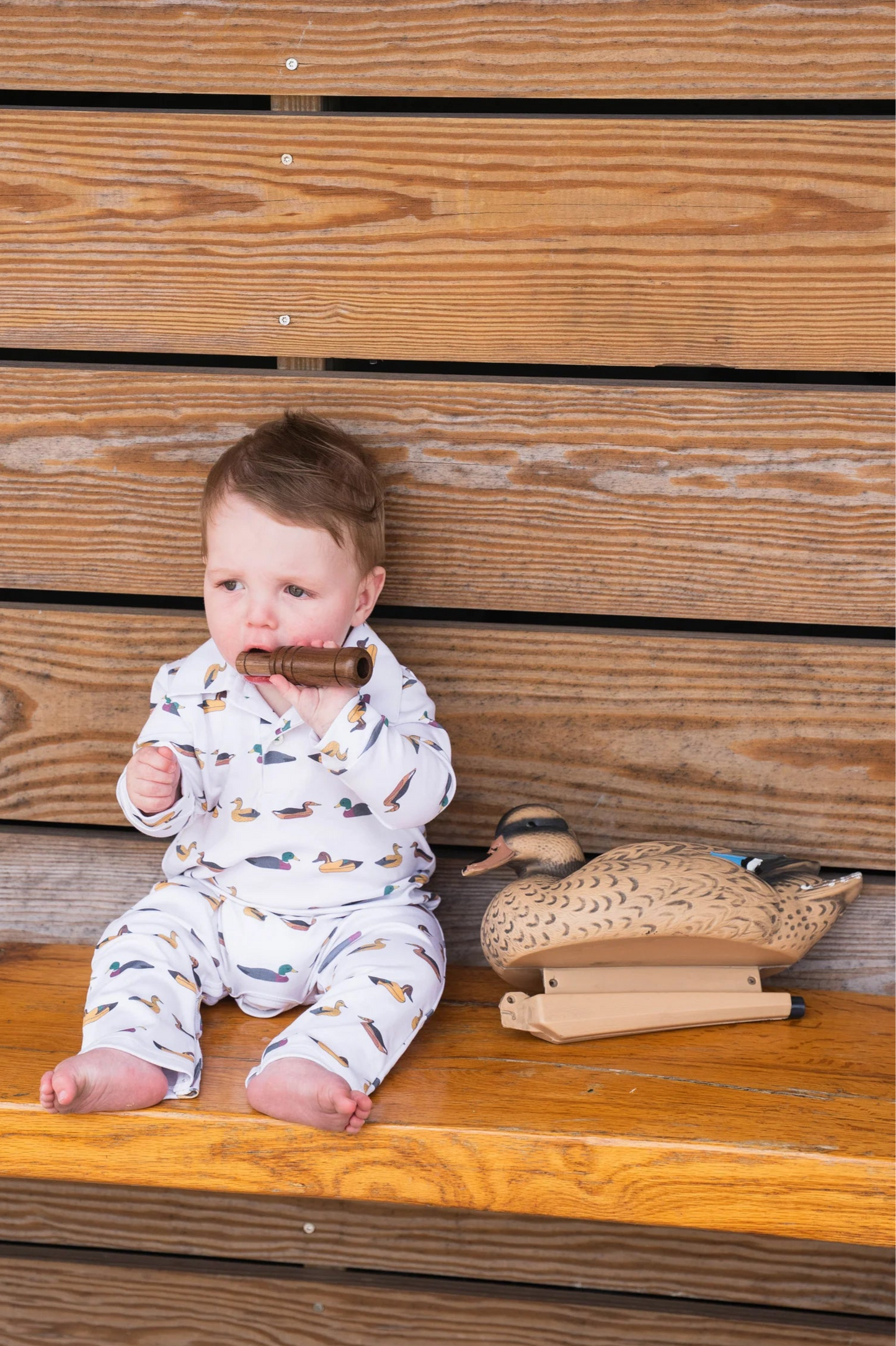Baby wearing SBC Signature Polo Long-Sleeve Romper, sitting and holding a duck call, highlighting soft, breathable fabric and playful style.