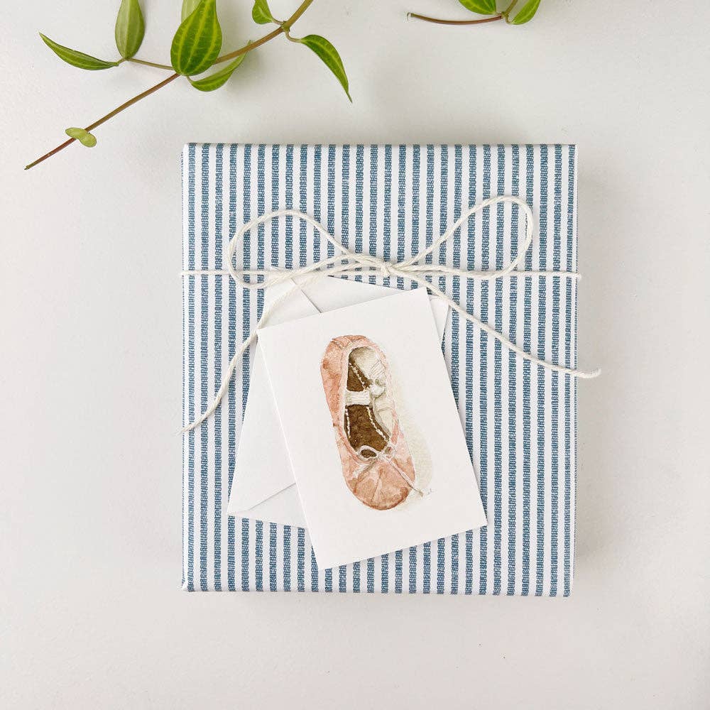 Close-up of the Emily Lex watercolor ballet shoe tiny notecard resting atop a beautifully wrapped gift, showcasing its delicate design. Did you know that at Grace & Haven, we wrap all gifts for free? This charming notecard adds a personal and artistic touch to any gift, making it perfect for ballet lovers or anyone who appreciates fine art. Ideal for accompanying a gift for a birthday, celebration, or special occasion, with thoughtful details that show you care.