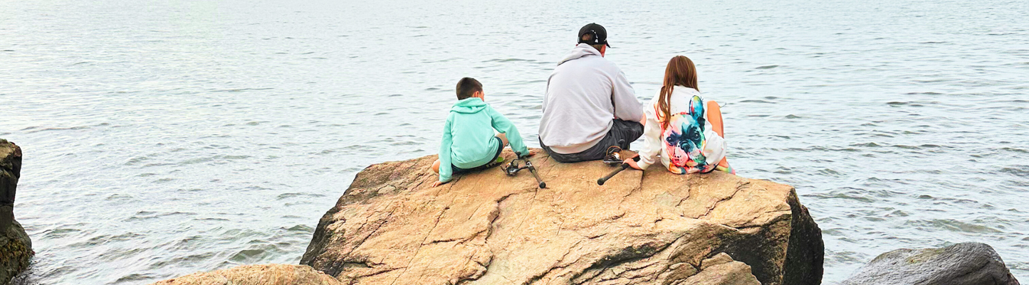Two children sitting on a rock by the water, fishing together, capturing a quiet family moment in nature