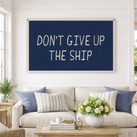 Canvas banner tapestry with navy background and white text reading Don't Give Up The Ship hanging on a white wall above a