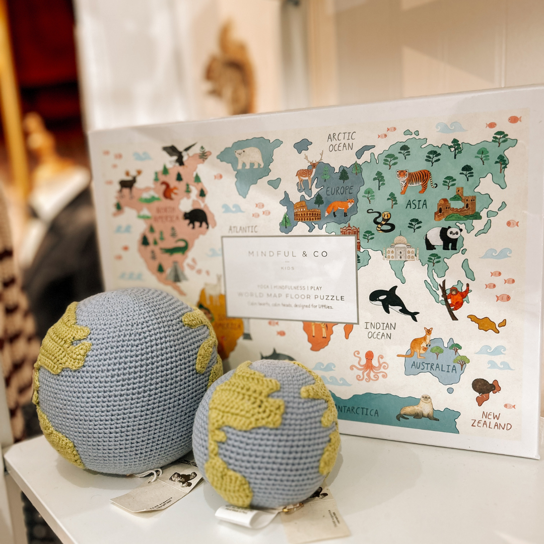 Mindful & Co Kids World Floor Puzzle and crocheted organic globe rattles on a shelf at Grace & Haven, showcasing high-quality, thoughtful children’s products.