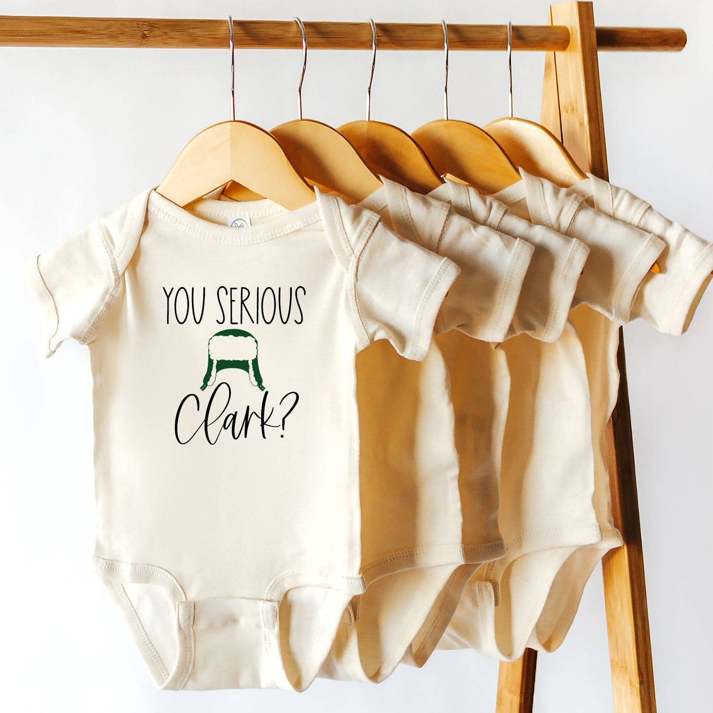 Hanging view of the "Are You Serious Clark" onesies, featuring a playful and fun holiday-themed design. These soft, comfortable onesies are perfect for your little one during the festive season. Crafted from high-quality fabric, they offer a cozy fit while showcasing a humorous reference to the classic holiday movie. Ideal for family photos, holiday gifts, or lounging at home, this onesie combines comfort with a touch of seasonal fun.