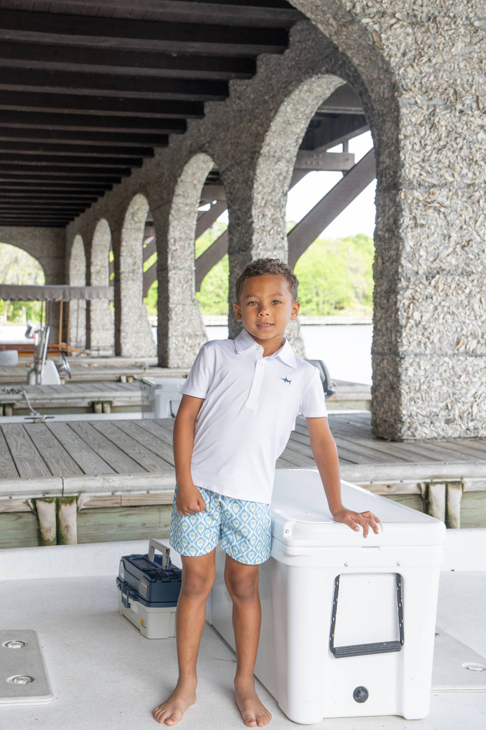 A young boy wearing the Saltwater Boys white polo, ready for a fun day of fishing. The comfortable, classic polo is perfect for outdoor adventures and is a must-have for summer activities.