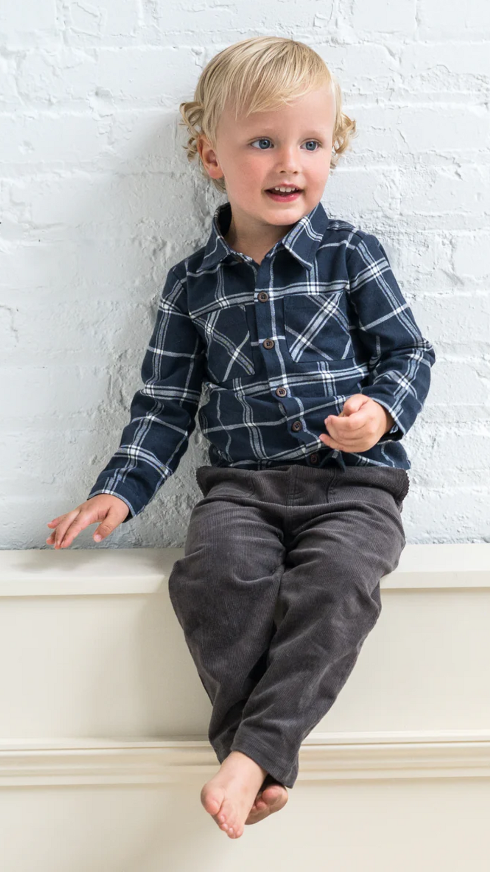 A toddler boy wearing a navy plaid flannel shirt, smiling in a studio setting, highlighting the shirt’s cozy fit and versatile style.