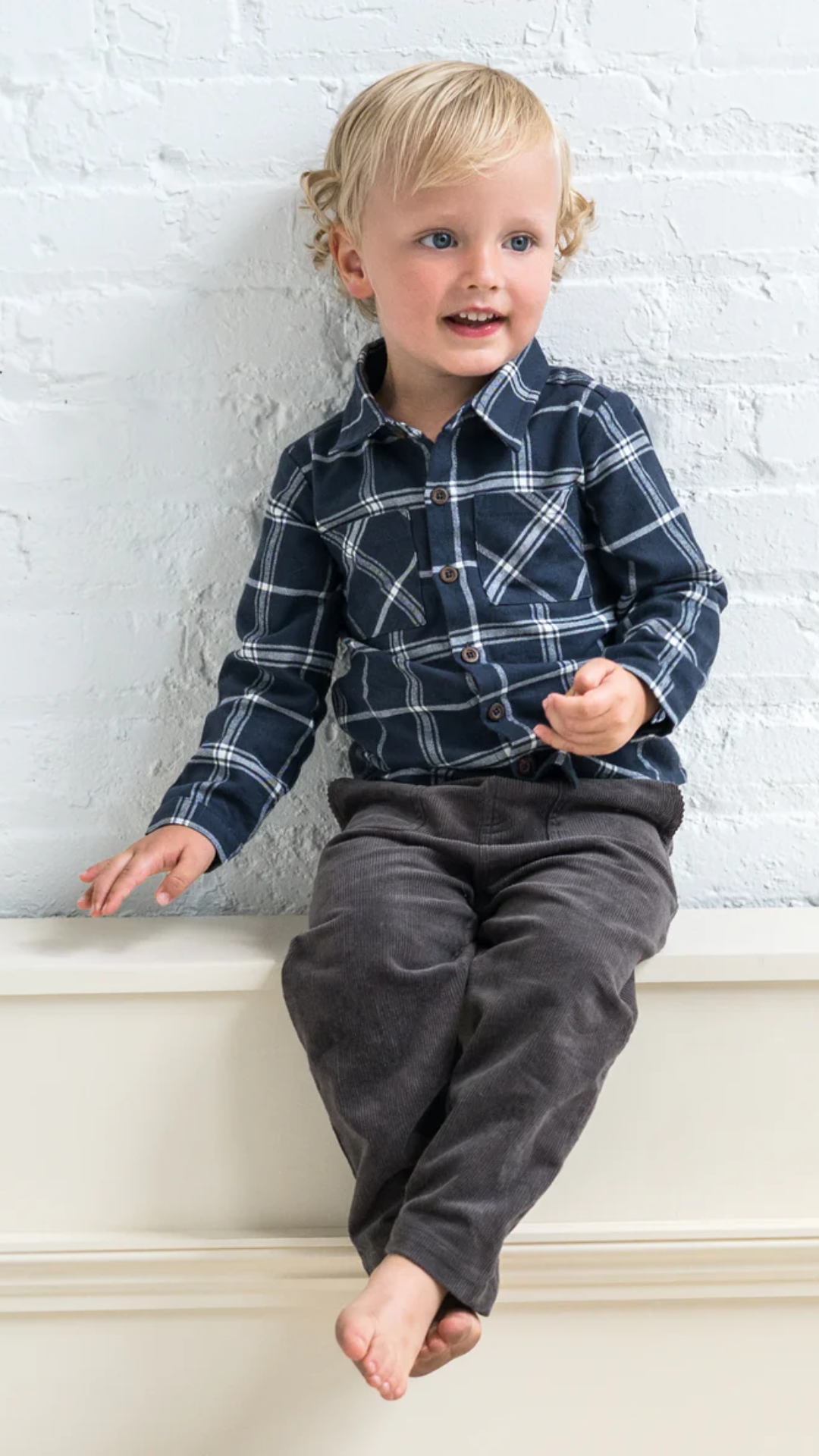 A toddler boy wearing a navy plaid flannel shirt, smiling in a studio setting, highlighting the shirt’s cozy fit and versatile style.