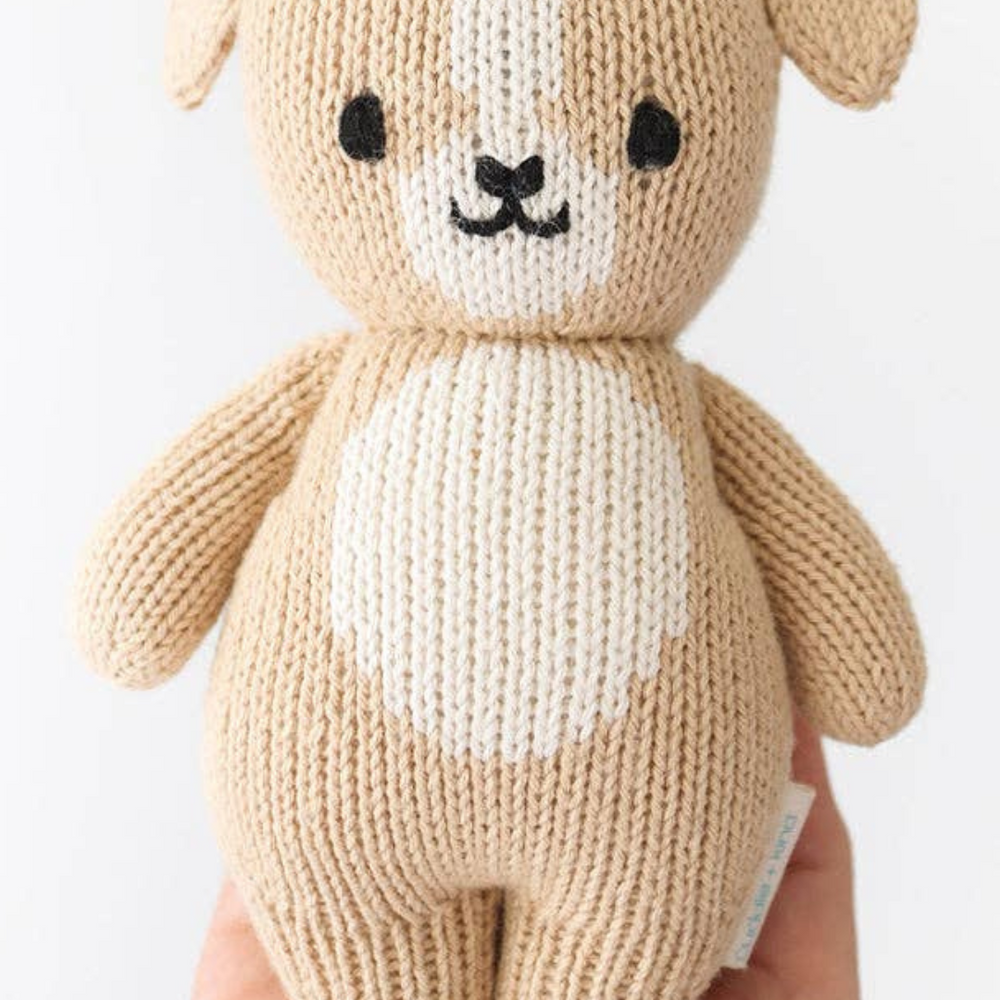 Close-up of the Baby Puppy from Cuddle + Kind, perfectly sized to fit in the palm of a hand, showcasing its softness and handcrafted details with natural cotton yarn.