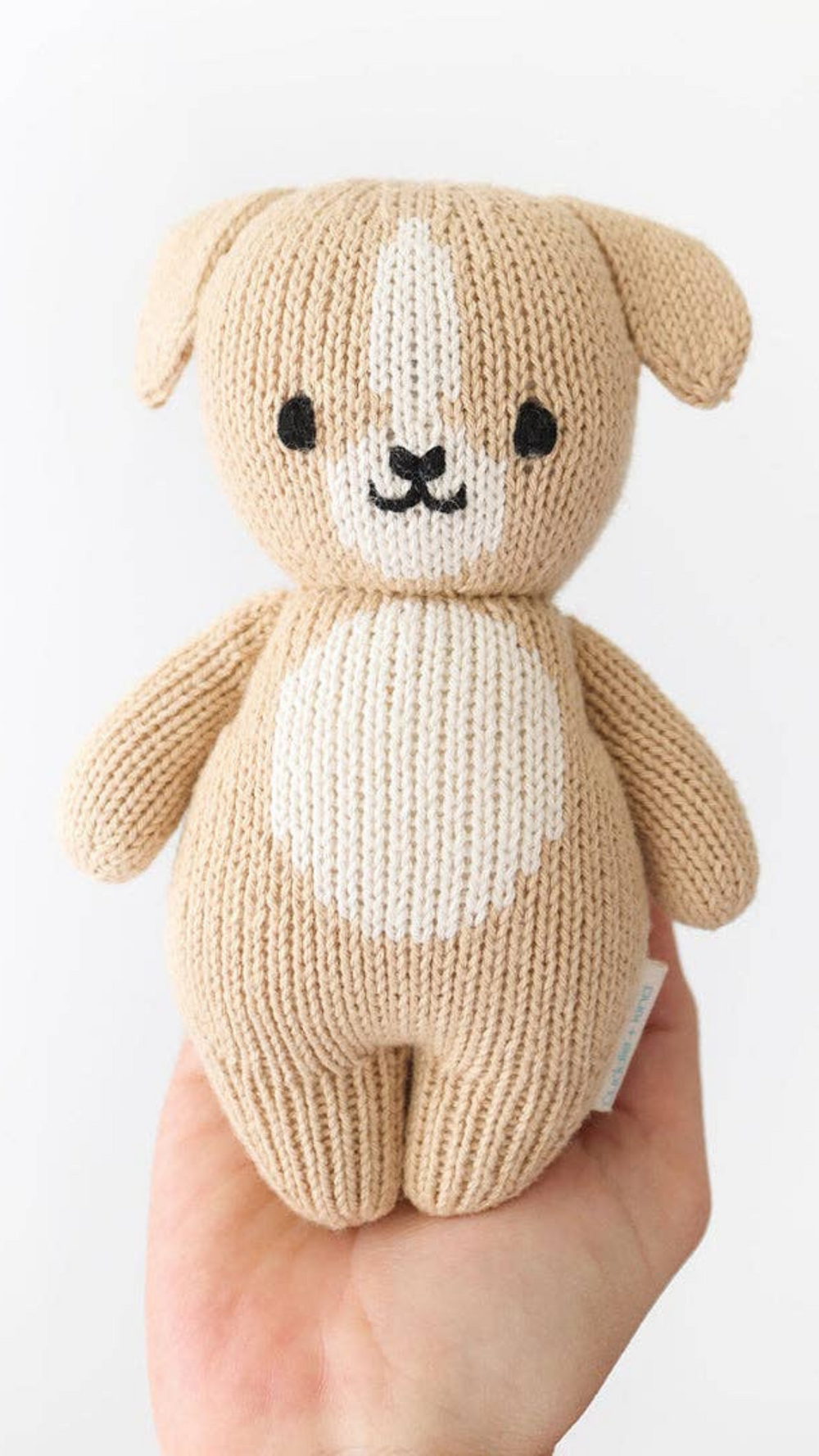 Close-up of the Baby Puppy from Cuddle + Kind, perfectly sized to fit in the palm of a hand, showcasing its softness and handcrafted details with natural cotton yarn.