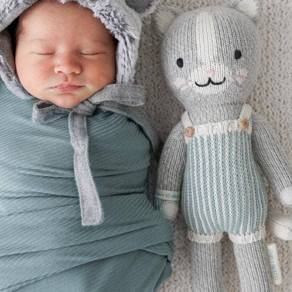 Swaddled baby with Dylan the Kitten in Little size (13”), highlighting the softness and comfort of this hand-knit, eco-friendly doll.