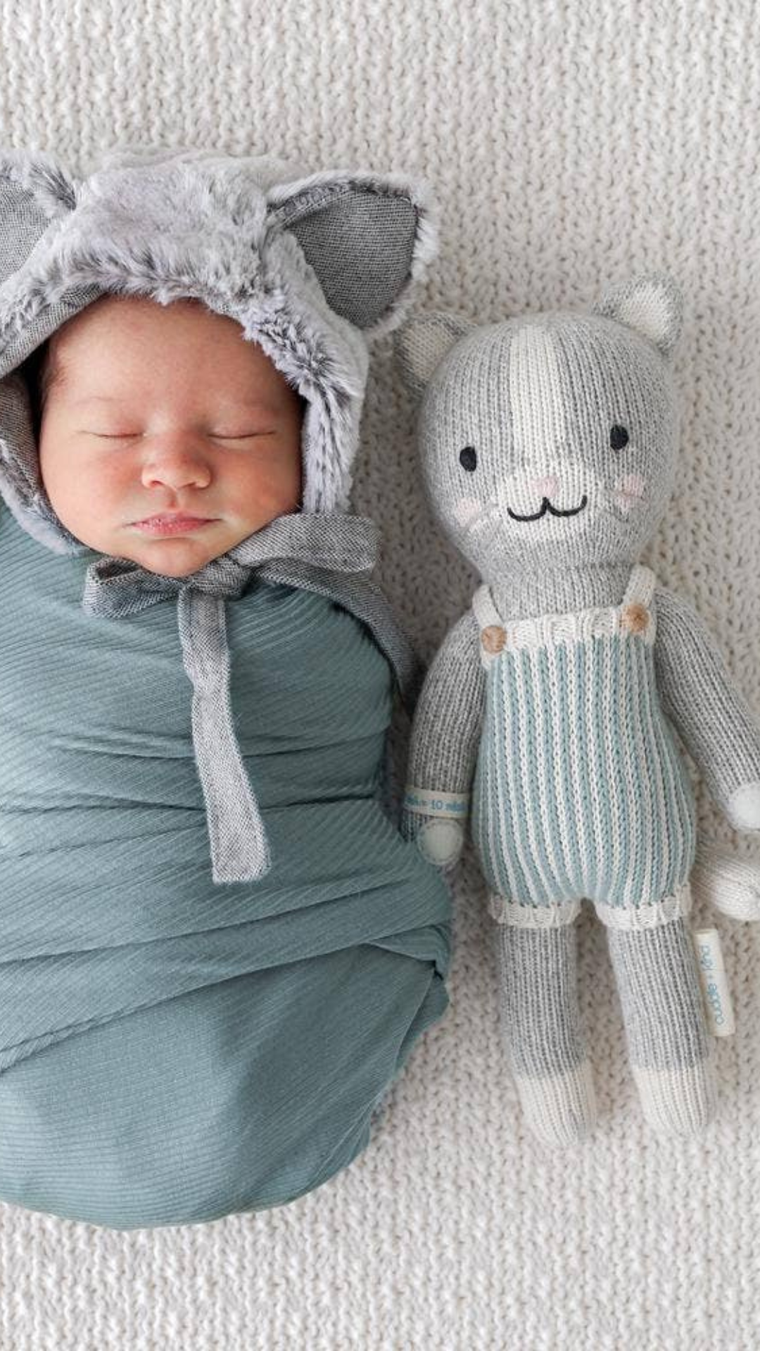 Swaddled baby with Dylan the Kitten in Little size (13”), highlighting the softness and comfort of this hand-knit, eco-friendly doll.