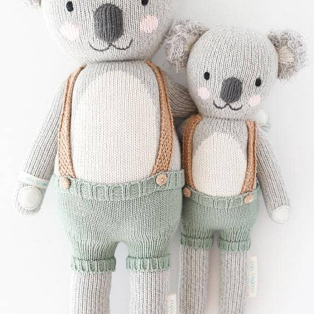 Flatlay of Quinn the Koala doll in Little (13”) and Regular (20”) sizes with soft colors, showcasing heirloom-quality hand-knit craftsmanship.