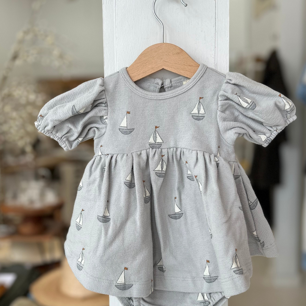 
                      
                        Featuring a delicate sailboat print on a soft, muted blue background, this dress brings a sweet nautical touch to any occasion.
                      
                    