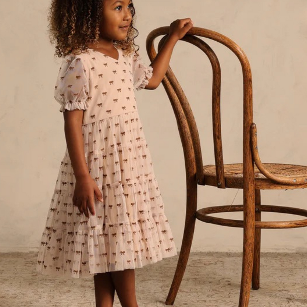 
                      
                        Toddler wearing The Dottie Dress in a studio – Toddler confidently modeling The Dottie Dress by Noralee in a studio setting, showcasing the dress’s comfortable fit and delightful bow details, ideal for playful moments.
                      
                    