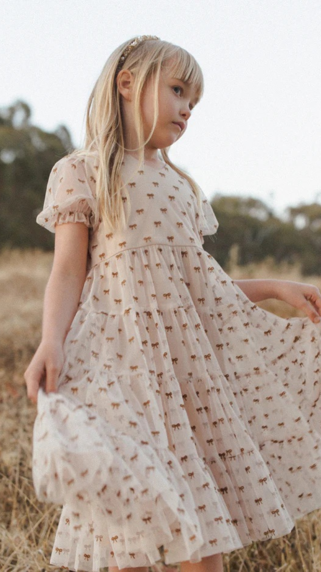 Girl twirling in The Dottie Dress by Noralee – A young girl twirls joyfully in The Dottie Dress by Noralee, showcasing its playful bow pattern and puff sleeves, perfect for special occasions and everyday style.