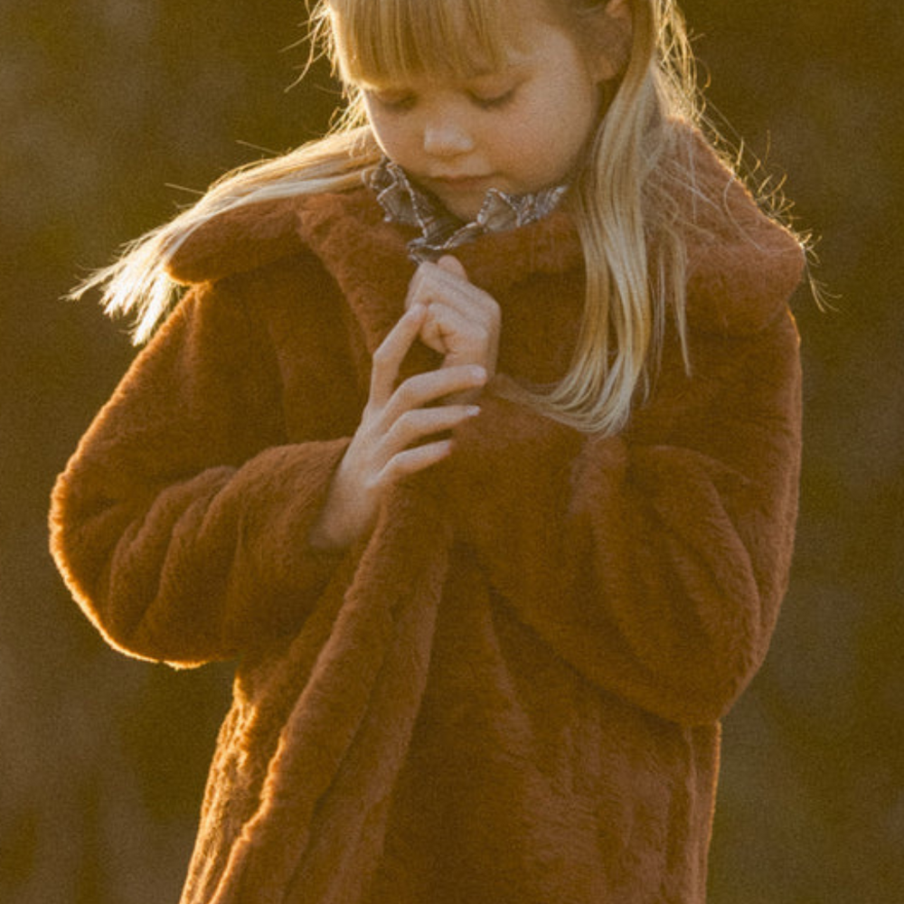 
                      
                        Girl in field at golden hour wearing the warm Eloise Coat in Copper, capturing cozy and fashionable outerwear for kids on chilly days.
                      
                    