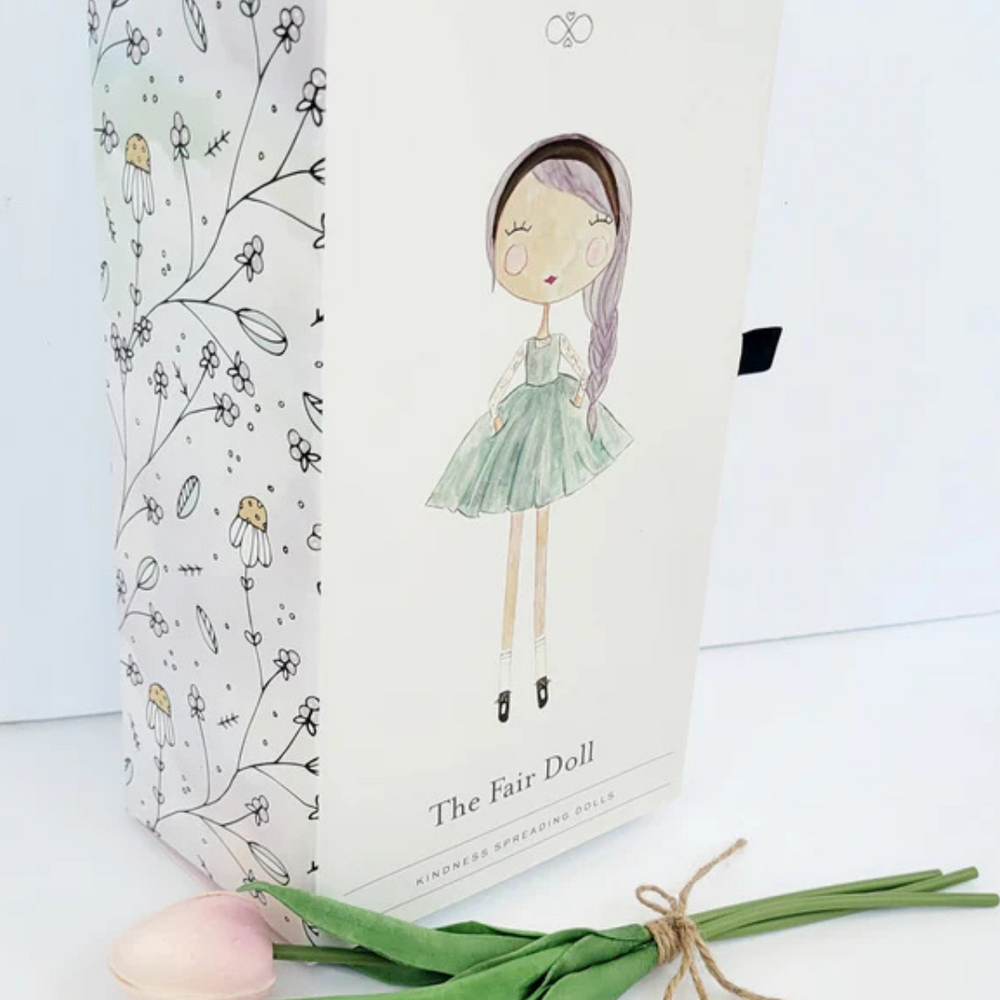 
                      
                        Showcasing the beautiful box packaging of the Fair Kindness Doll beside pale pink tulips, perfect for gifting and special occasions.
                      
                    