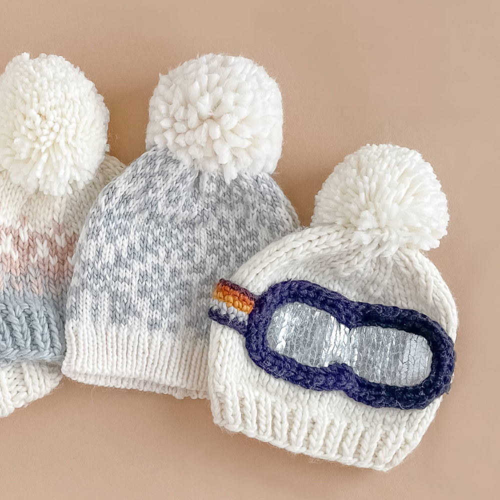 
                      
                        Close-up of Ski Goggles Hat pom-pom and detailed goggle band in navy, mustard, cinnamon, and grey, adding flair to winter outfits.
                      
                    