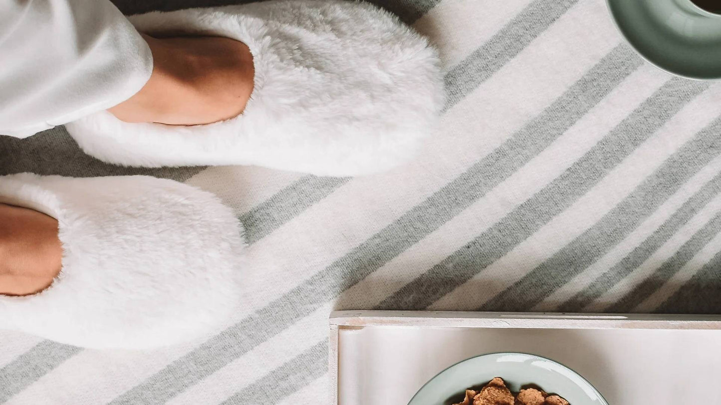Person wearing slippers on a striped rug with a bowl of food nearby. Our get cozy collection is perfect for keeping warm this winter.