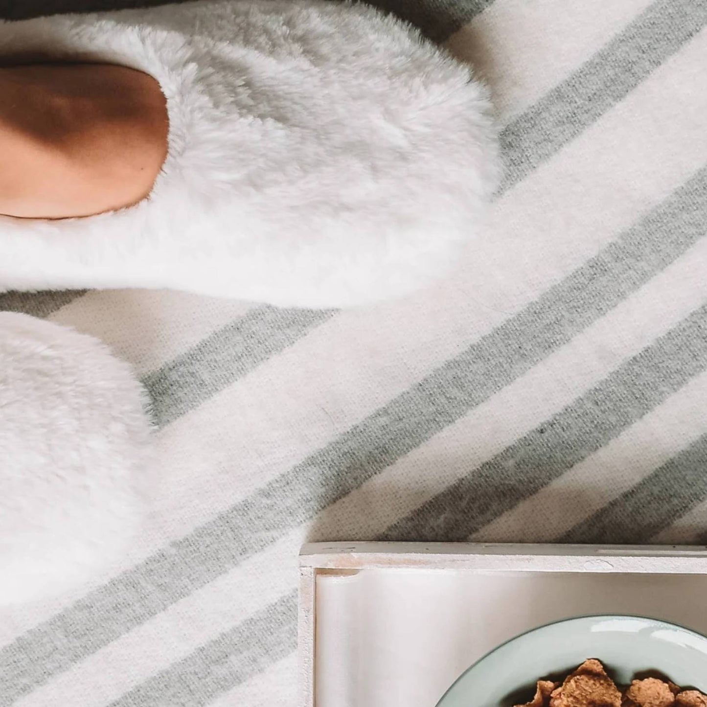 Fuzzy slippers with microwavable inserts cozied up by a breakfast tray in soft morning light.