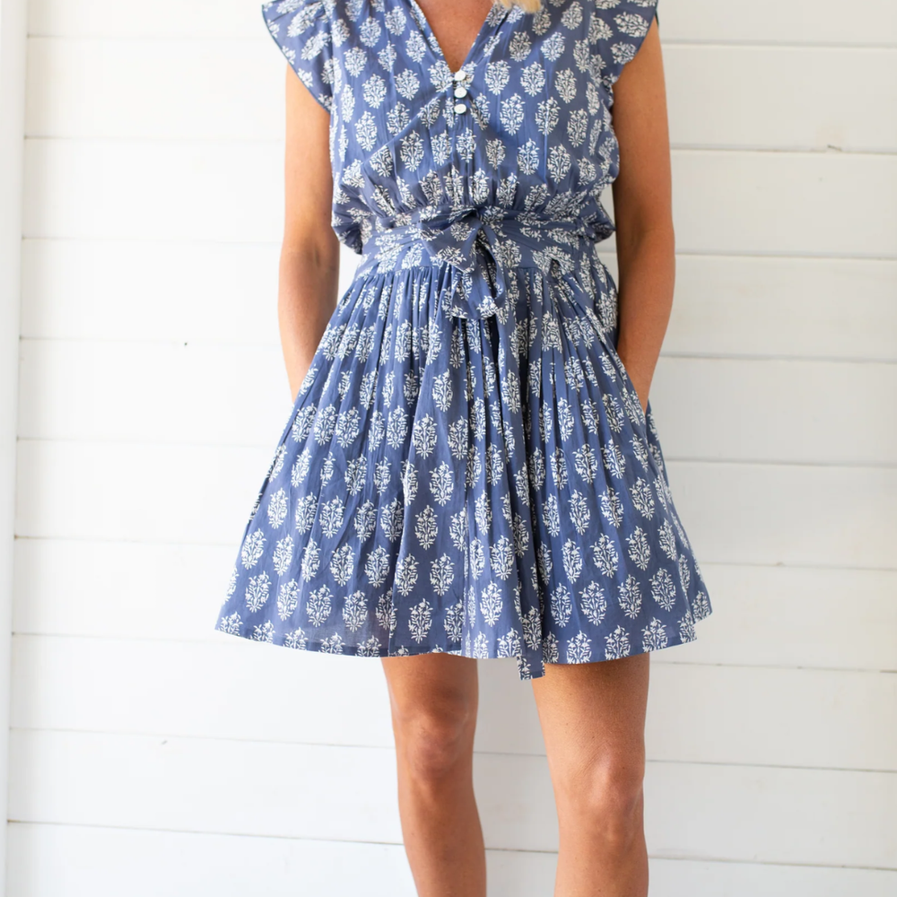 
                      
                        Playful Liz dress with a smocked back, functional pockets, tie feature, and shell button embellishments, perfect for sunny days
                      
                    