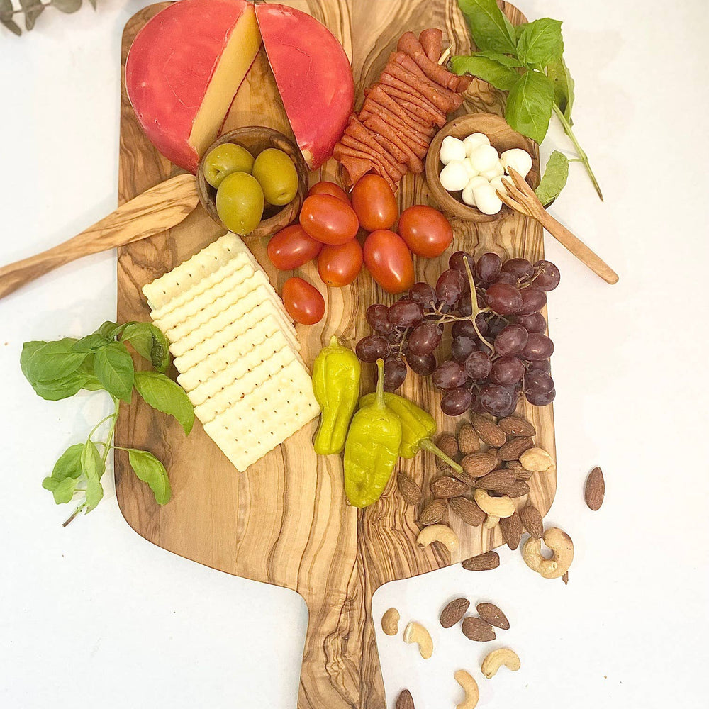 
                      
                        Overhead view of an olive wood charcuterie board beautifully arranged with an assortment of cheeses, meats, fruits, and nuts. This stylish and sustainable board is perfect for hosting gatherings and adding a touch of elegance to your next party or event. The natural wood grain of the olive wood enhances the presentation, making it an eye-catching centerpiece for any occasion. Ideal for those who appreciate quality, craftsmanship, and a delicious spread.
                      
                    