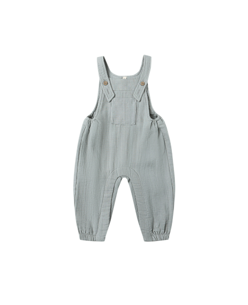 Flatlay of the Quincy Mae Baby Overalls in Steel Blue, made from 100% organic cotton, featuring adjustable straps with coconut button closures, an open bib pocket, and snap leg closures for easy changes.
