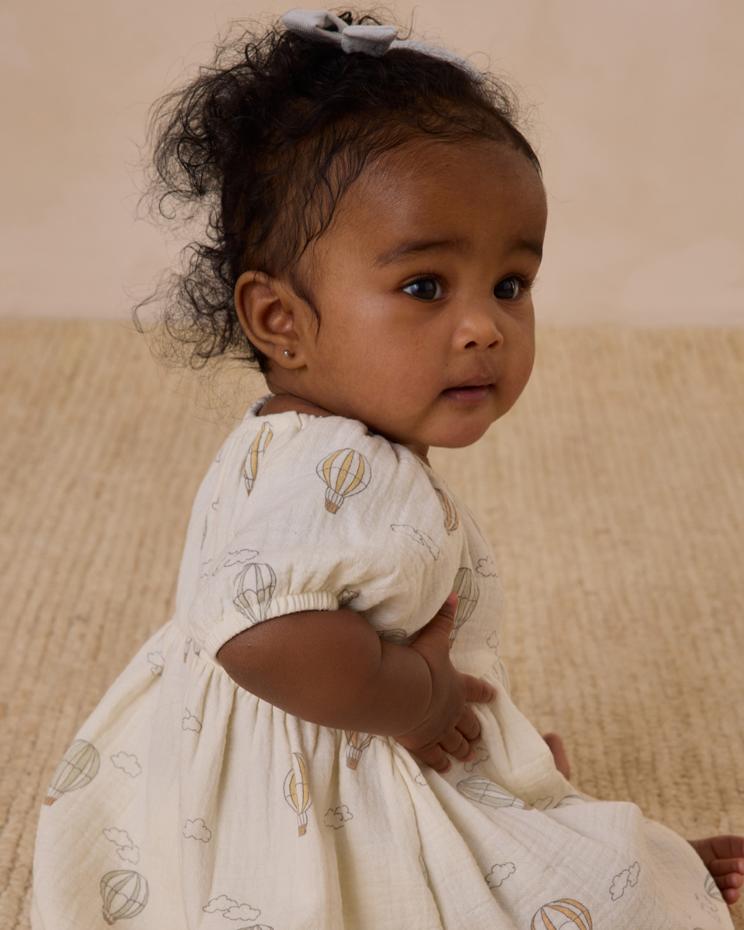 A charming side profile of a baby wearing the Quincy Mae Bella Dress, showcasing its whimsical hot air balloon print, delicate ruffle sleeves, and flowy silhouette, perfect for warm-weather adventures.