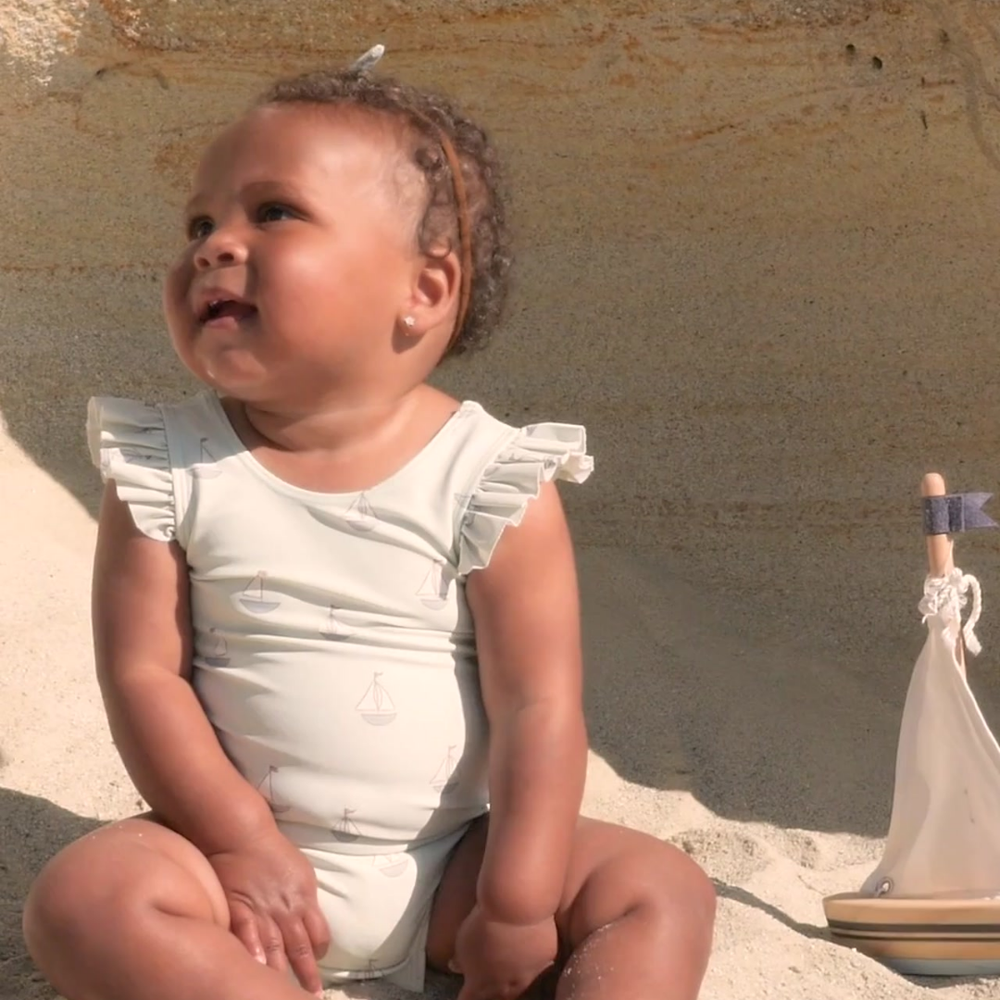 A sweet video of a baby enjoying the beach in the Scoop Back One-Piece Swimsuit - Sailboats, featuring a nautical sailboat print, flutter sleeves, and a stylish scoop back. Made from soft, quick-drying fabric with UPF protection, perfect for sun-soaked adventures.