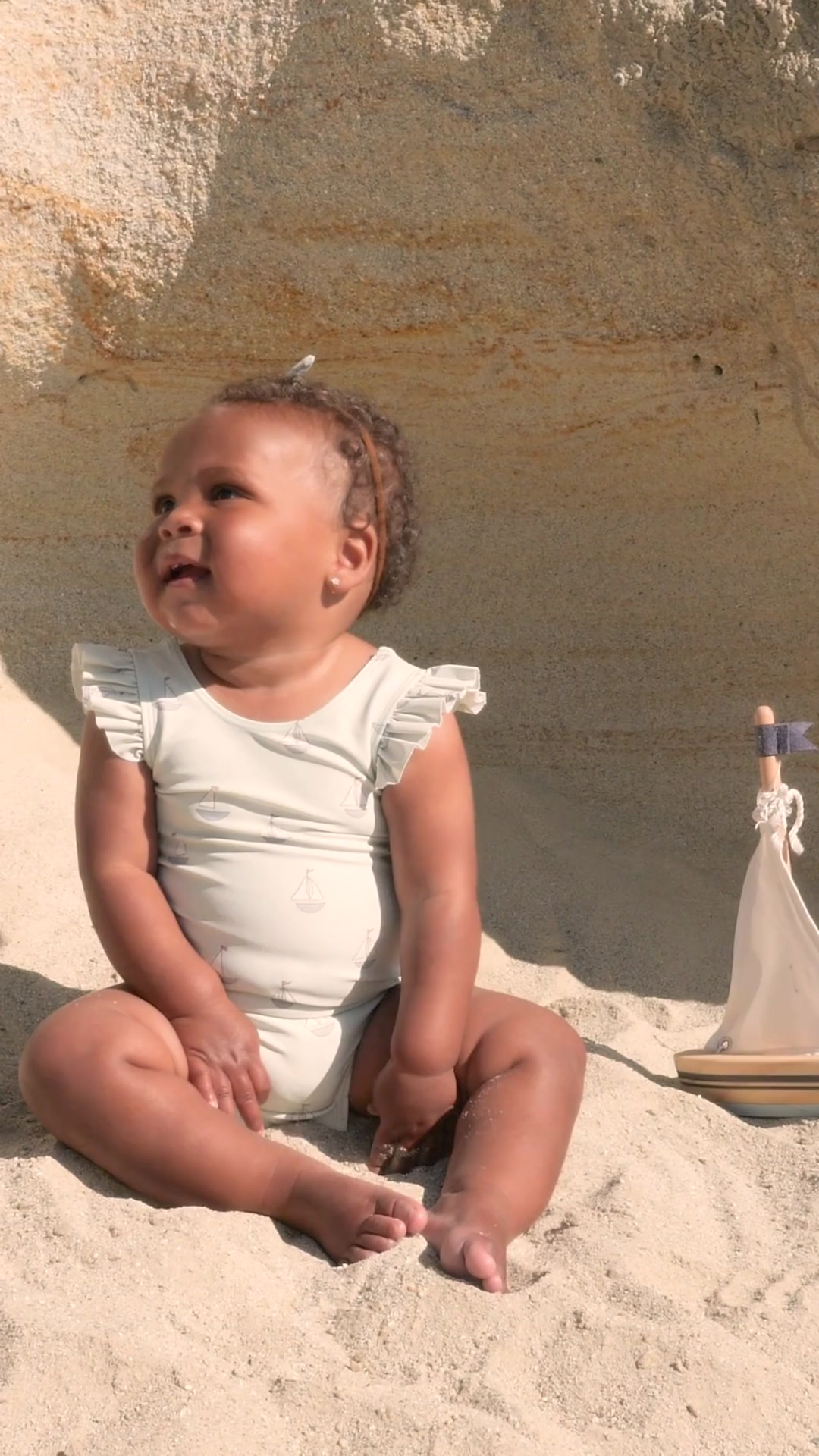 A sweet video of a baby enjoying the beach in the Scoop Back One-Piece Swimsuit - Sailboats, featuring a nautical sailboat print, flutter sleeves, and a stylish scoop back. Made from soft, quick-drying fabric with UPF protection, perfect for sun-soaked adventures.