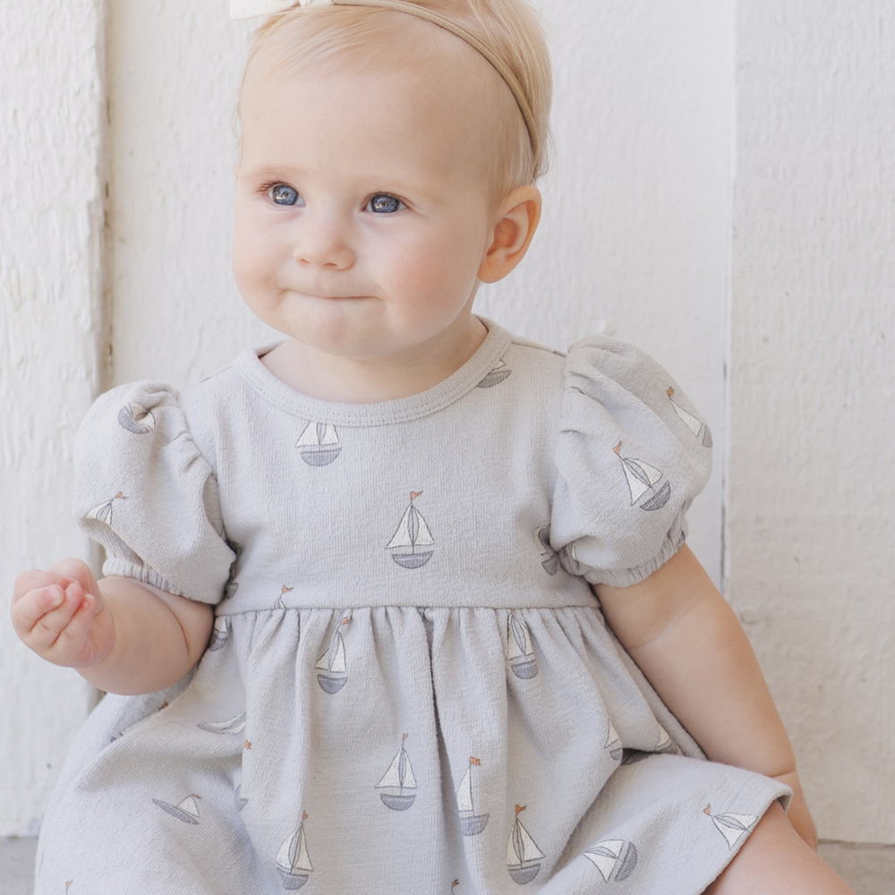 
                      
                        A full view of a baby in the Quincy Mae dress, featuring a timeless, cozy design made from breathable, organic fabric for all-day comfort.
                      
                    