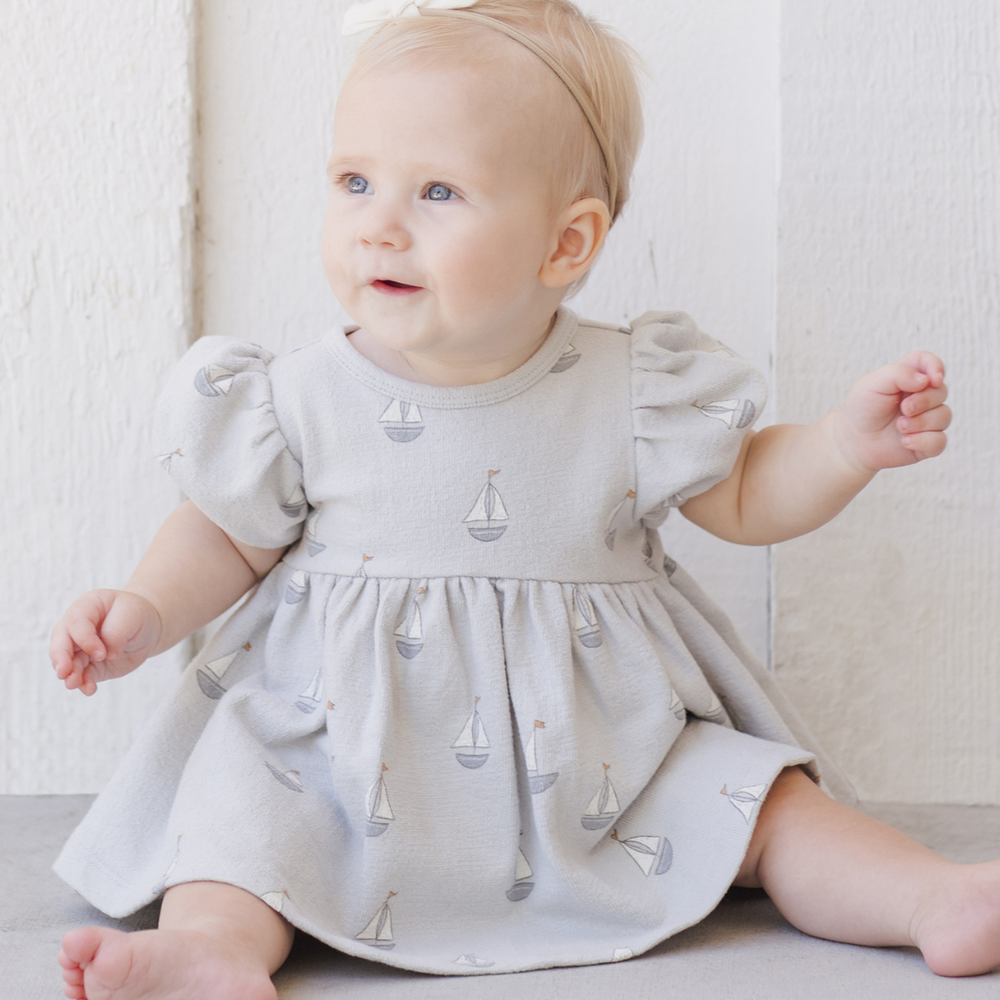 An adorable baby sitting while wearing the Quincy Mae dress, highlighting its flowy silhouette and charming details, ideal for everyday wear or special occasions.