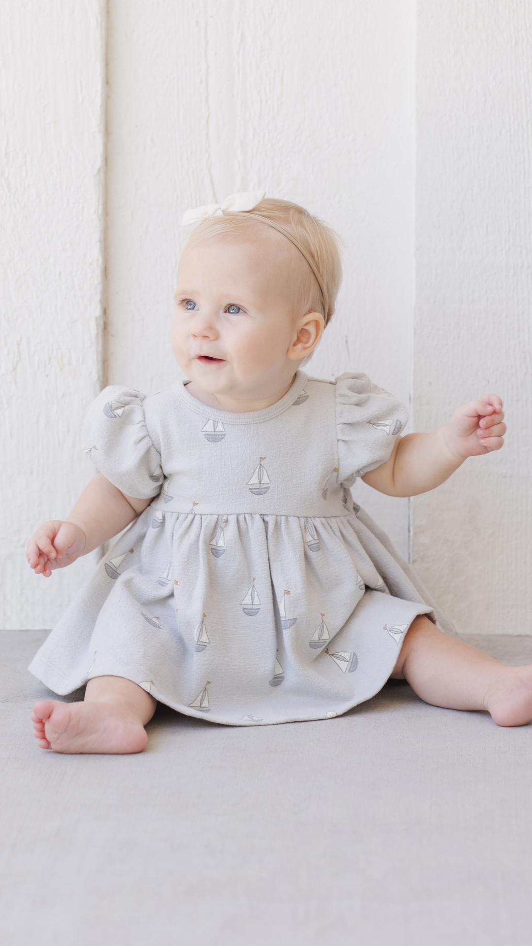 An adorable baby sitting while wearing the Quincy Mae dress, highlighting its flowy silhouette and charming details, ideal for everyday wear or special occasions.